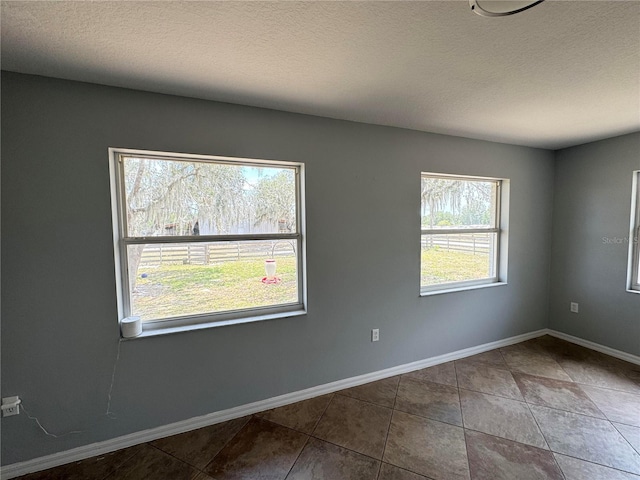 unfurnished room with a healthy amount of sunlight, a textured ceiling, and dark tile flooring