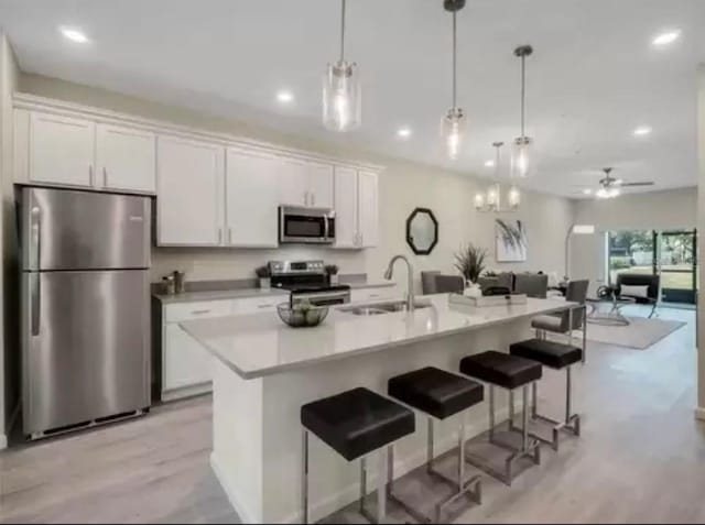 kitchen with a center island with sink, light countertops, appliances with stainless steel finishes, white cabinetry, and a sink