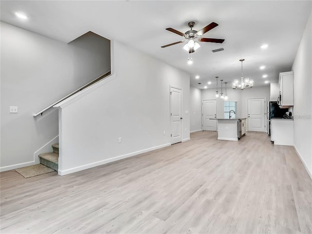 unfurnished living room with light wood finished floors, visible vents, stairway, a sink, and ceiling fan with notable chandelier