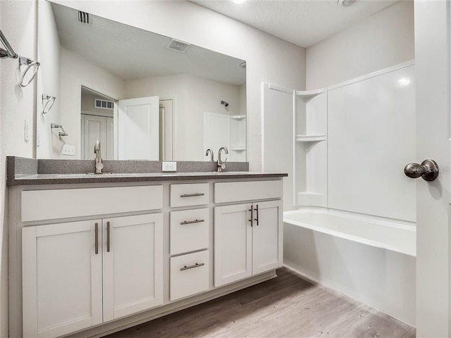 bathroom with a sink, wood finished floors, visible vents, double vanity, and washtub / shower combination