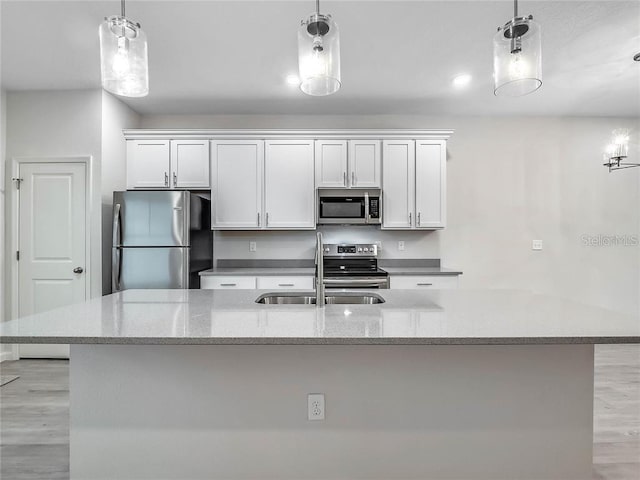 kitchen with stainless steel appliances, hanging light fixtures, white cabinetry, a sink, and light stone countertops