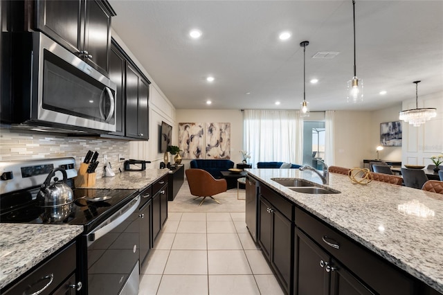 kitchen with appliances with stainless steel finishes, sink, pendant lighting, light stone countertops, and tasteful backsplash