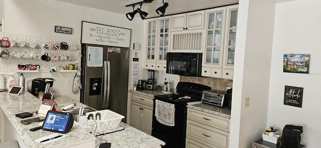 kitchen with cream cabinetry, black appliances, track lighting, a kitchen breakfast bar, and light stone countertops