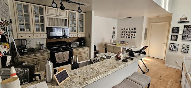 interior space featuring a breakfast bar, light stone countertops, light wood-type flooring, black appliances, and cream cabinets