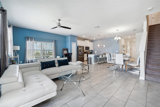 tiled living room with ceiling fan with notable chandelier