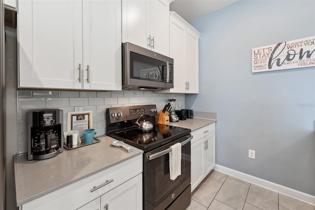 kitchen with light tile floors, black electric range oven, white cabinets, backsplash, and light stone counters