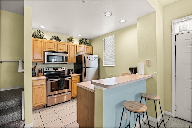 kitchen featuring a kitchen breakfast bar, appliances with stainless steel finishes, light brown cabinets, and light tile flooring