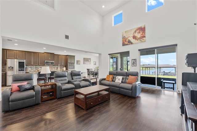 living room featuring dark wood-type flooring, a towering ceiling, and a water view