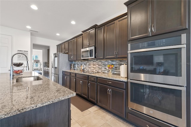 kitchen with appliances with stainless steel finishes, sink, tasteful backsplash, light tile flooring, and light stone countertops