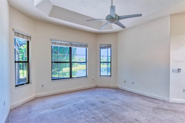 empty room with light colored carpet, plenty of natural light, ceiling fan, and a raised ceiling