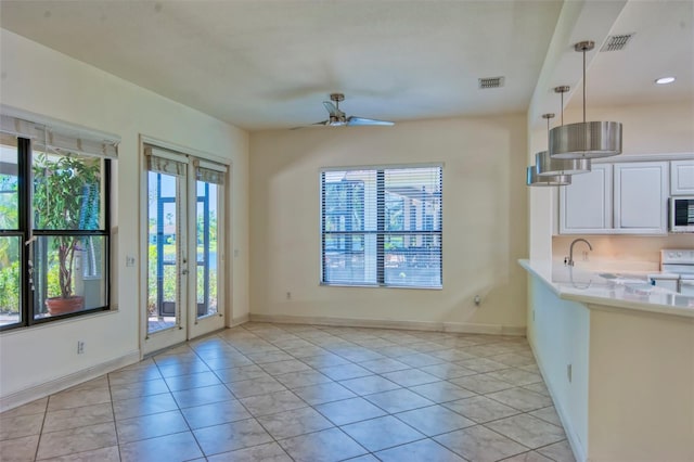 interior space featuring ceiling fan, light tile flooring, pendant lighting, stainless steel microwave, and white cabinets