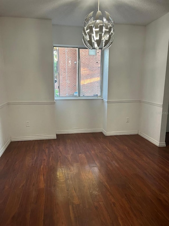 unfurnished room featuring dark hardwood / wood-style flooring, a textured ceiling, and a notable chandelier