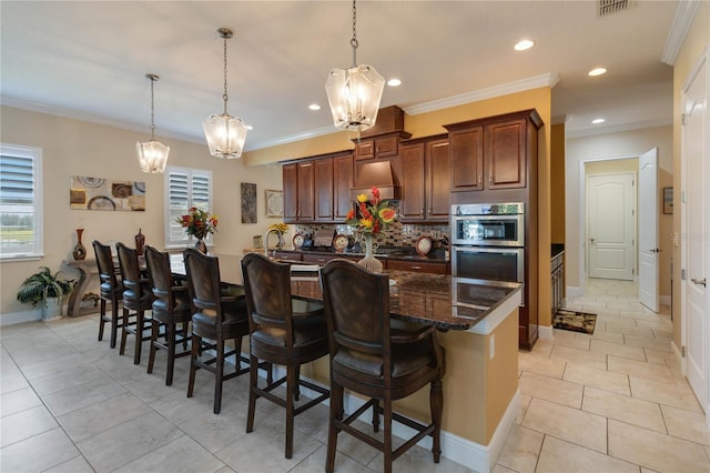 kitchen featuring light tile floors, double oven, backsplash, decorative light fixtures, and a kitchen breakfast bar