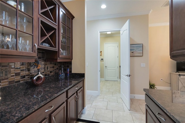 kitchen with crown molding, dark brown cabinets, light tile floors, tasteful backsplash, and dark stone counters