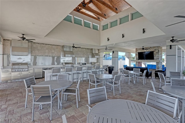 view of patio featuring exterior kitchen, ceiling fan, a stone fireplace, and area for grilling