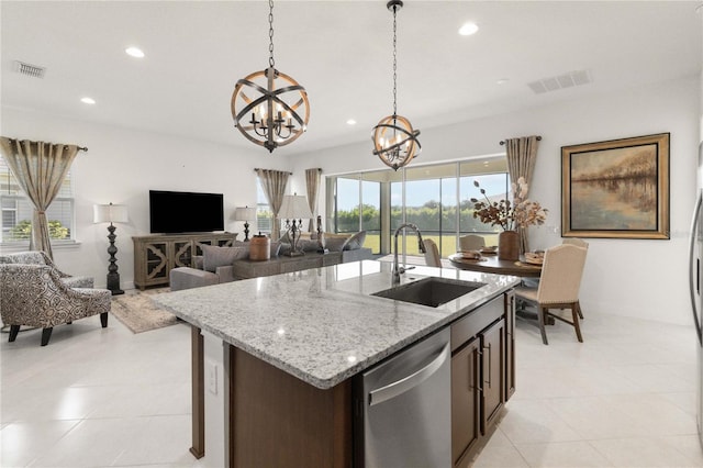 kitchen with decorative light fixtures, light tile floors, sink, and an island with sink