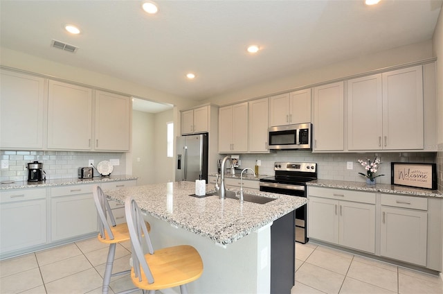 kitchen with a kitchen island with sink, light stone countertops, light tile patterned flooring, a kitchen bar, and stainless steel appliances