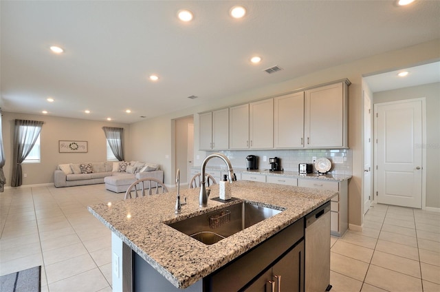 kitchen featuring light stone countertops, tasteful backsplash, stainless steel dishwasher, sink, and an island with sink