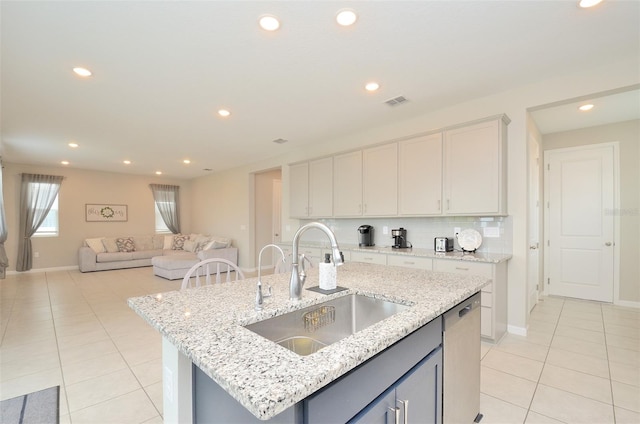 kitchen featuring tasteful backsplash, light stone counters, a kitchen island with sink, sink, and dishwasher