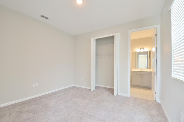 unfurnished bedroom featuring connected bathroom, light carpet, a closet, and sink