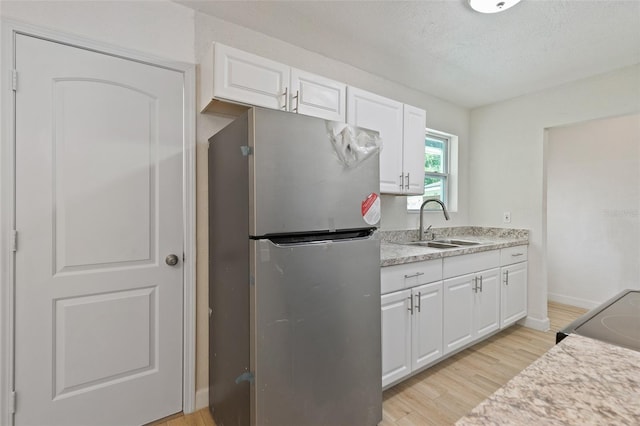 kitchen with light stone countertops, light wood-type flooring, white cabinetry, sink, and stainless steel fridge