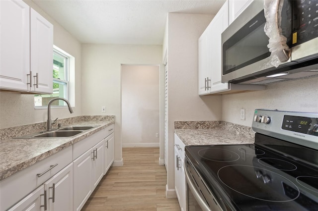 kitchen with sink, stainless steel appliances, light wood-type flooring, and white cabinetry