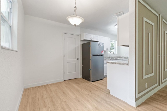 kitchen featuring decorative light fixtures, light stone countertops, light hardwood / wood-style flooring, white cabinetry, and stainless steel fridge