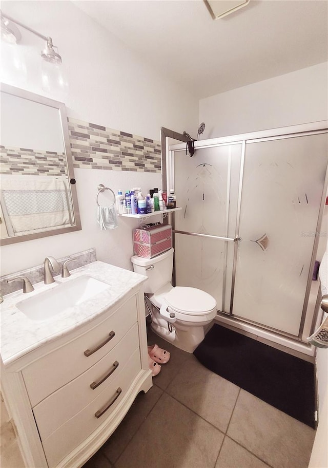 bathroom with tile flooring, oversized vanity, backsplash, toilet, and a shower with door