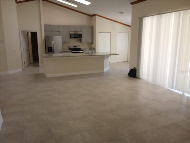 kitchen with stove, light tile flooring, gray cabinets, a center island with sink, and stainless steel fridge