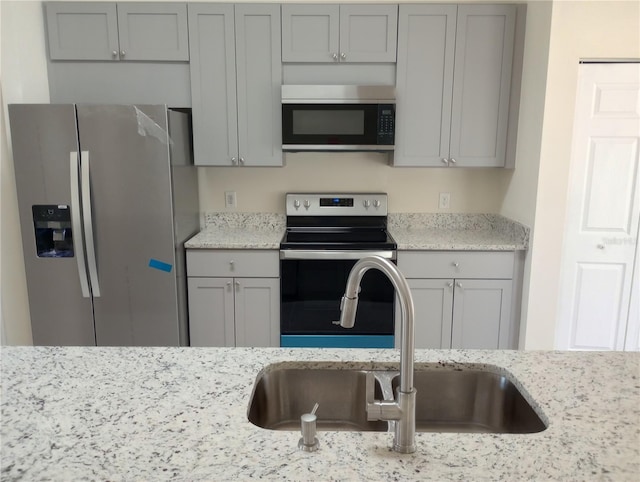 kitchen featuring sink, stainless steel appliances, light stone countertops, and gray cabinetry