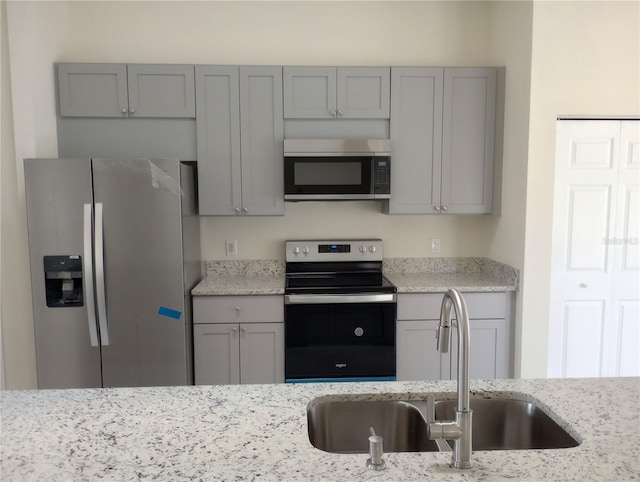 kitchen featuring appliances with stainless steel finishes, gray cabinetry, sink, and light stone counters