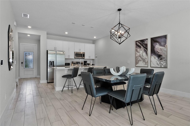 dining area featuring light hardwood / wood-style flooring, a textured ceiling, and a notable chandelier