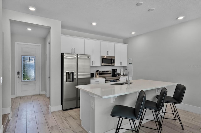 kitchen with appliances with stainless steel finishes, a kitchen island with sink, white cabinets, sink, and a breakfast bar