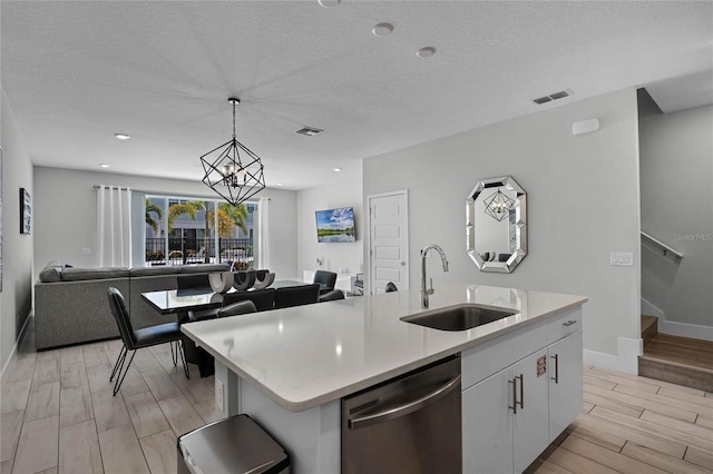 kitchen with sink, light wood-type flooring, stainless steel dishwasher, a center island with sink, and pendant lighting