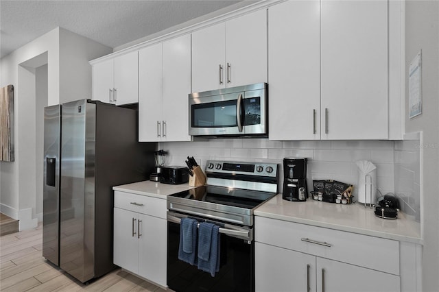 kitchen featuring white cabinets, backsplash, stainless steel appliances, light hardwood / wood-style floors, and a textured ceiling