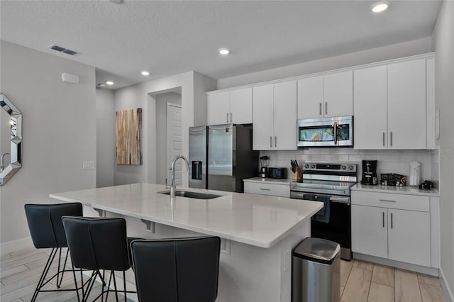 kitchen with backsplash, stainless steel appliances, white cabinetry, and a center island with sink