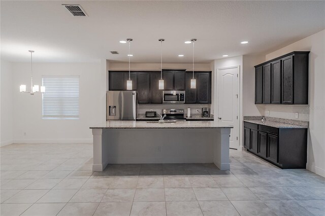 kitchen featuring light tile floors, decorative light fixtures, stainless steel appliances, a kitchen island with sink, and light stone countertops