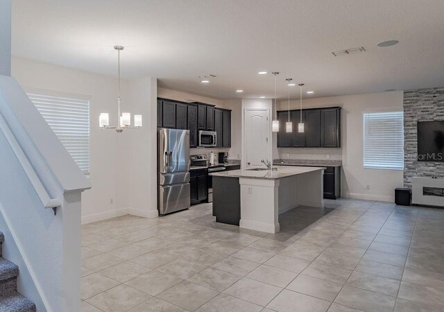 kitchen featuring light stone countertops, decorative light fixtures, appliances with stainless steel finishes, a center island with sink, and light tile flooring