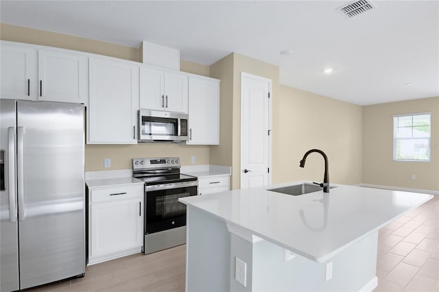 kitchen with white cabinets, stainless steel appliances, a kitchen island with sink, and sink