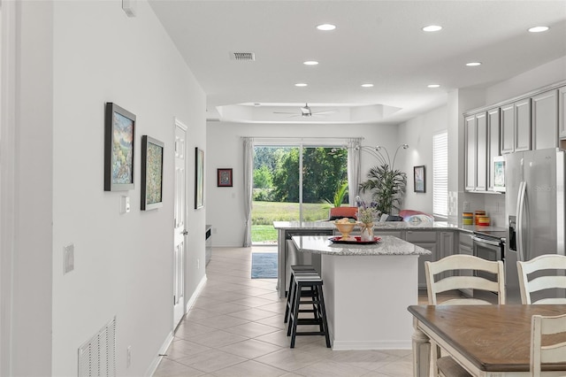 kitchen featuring gray cabinetry, a tray ceiling, appliances with stainless steel finishes, a kitchen bar, and ceiling fan