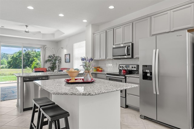 kitchen with backsplash, ceiling fan, stainless steel appliances, a center island, and light tile floors