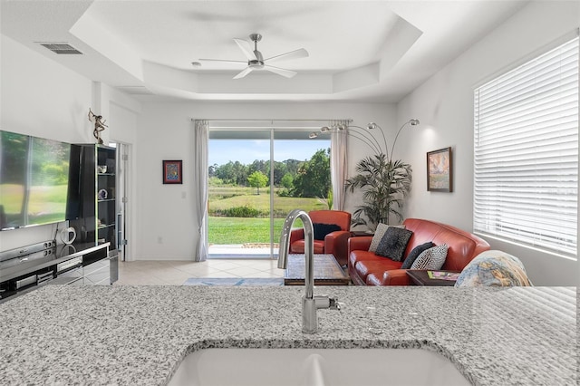 living room featuring sink, ceiling fan, light tile flooring, and a tray ceiling