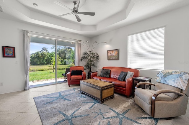 tiled living room with ceiling fan and a tray ceiling