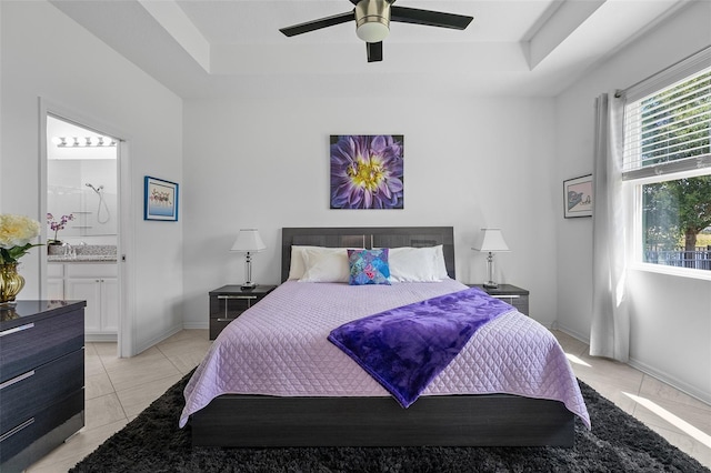 bedroom featuring a raised ceiling, ceiling fan, ensuite bathroom, and light tile floors