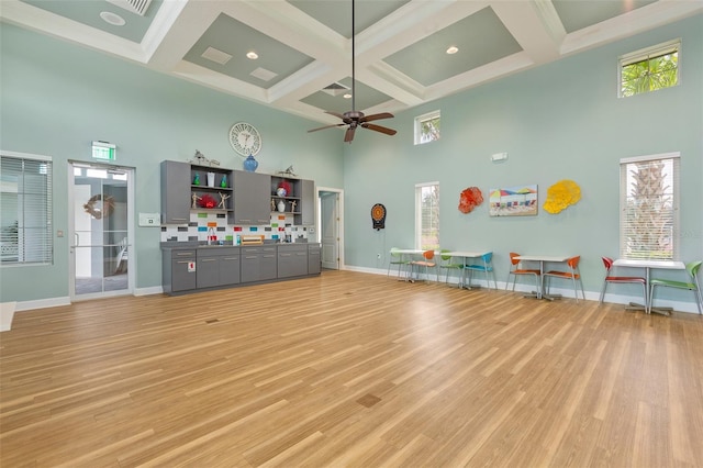 exercise room featuring ceiling fan, light wood-type flooring, a towering ceiling, and coffered ceiling