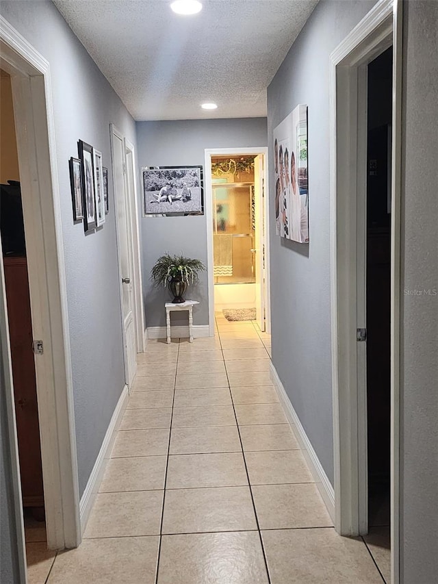 corridor featuring a textured ceiling and light tile floors