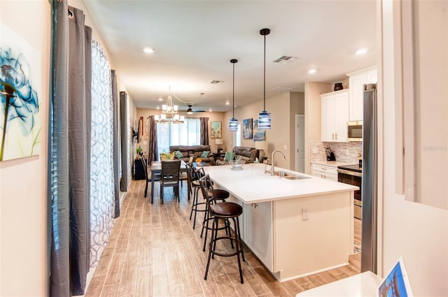 kitchen featuring sink, light wood-type flooring, white cabinetry, a breakfast bar area, and a kitchen island with sink