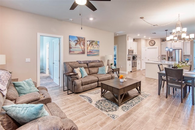 living room with sink, light hardwood / wood-style floors, and ceiling fan with notable chandelier