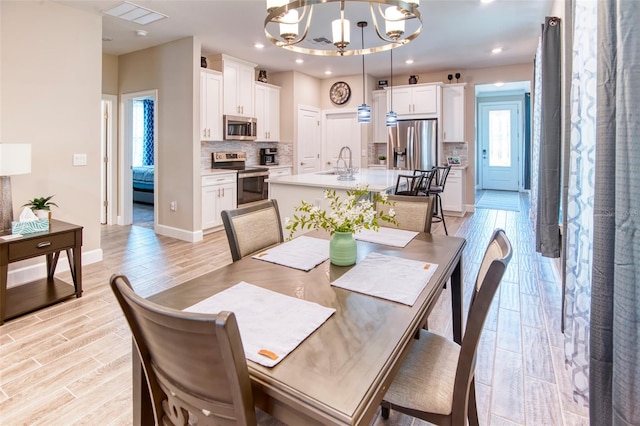 dining room with sink, light hardwood / wood-style flooring, and an inviting chandelier