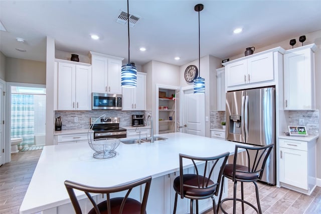 kitchen featuring hanging light fixtures, sink, stainless steel appliances, and a kitchen island with sink